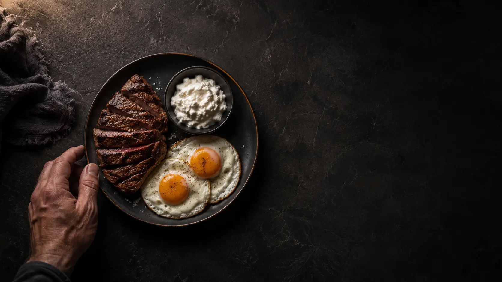 A high protein plate of steak, eggs and dairy on a dark counter, eating protein first to protect muscle on a GLP 1